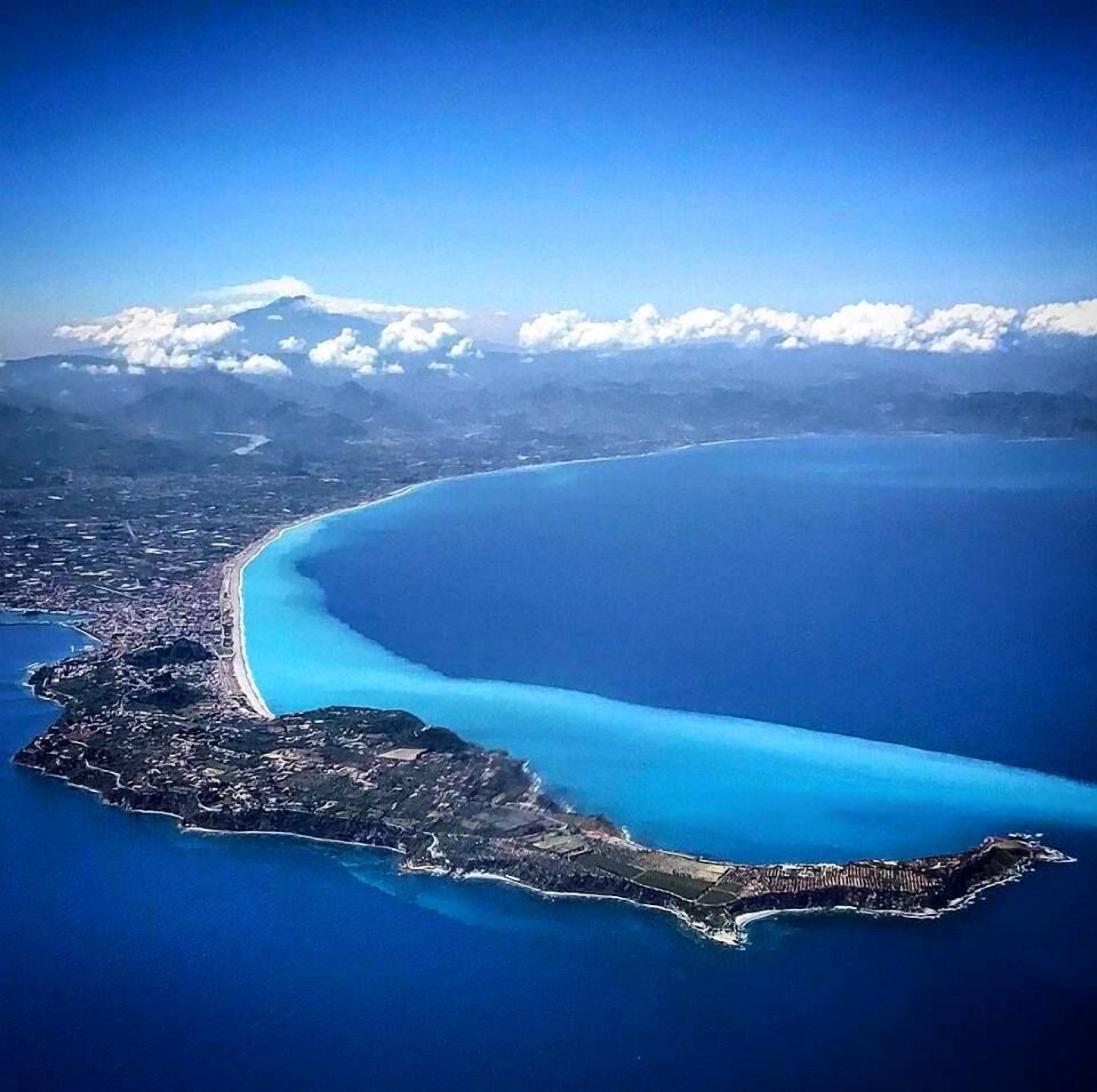 An aerial view of a coastal city with a large bay, a peninsula, and a mountain range in the background.
