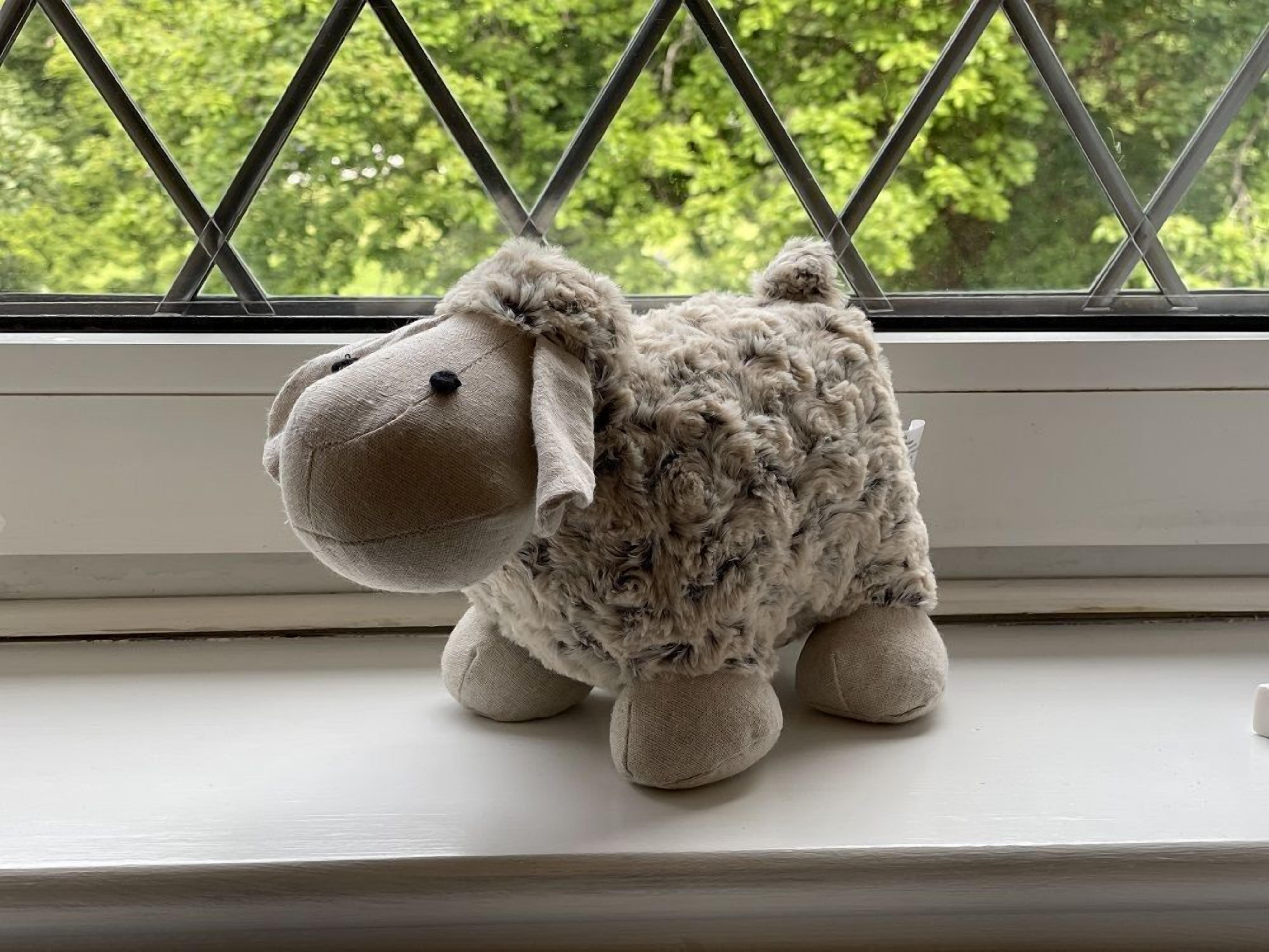 Ein plüschiges Schaf sitzt auf einer Fensterbank.