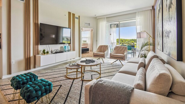 Un salon moderne avec un canapé, des poufs, un téléviseur et une vue sur l’extérieur.