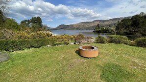 A grassy area with a circular stone structure, a lake, and hills in the background. - Brandlehow -  a house that sleeps 7 guests  in 4 bedrooms (Portinscale)