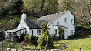 A white house with a large porch and a chimney, surrounded by a grassy area and trees. - Brandlehow -  a house that sleeps 7 guests  in 4 bedrooms (Portinscale)