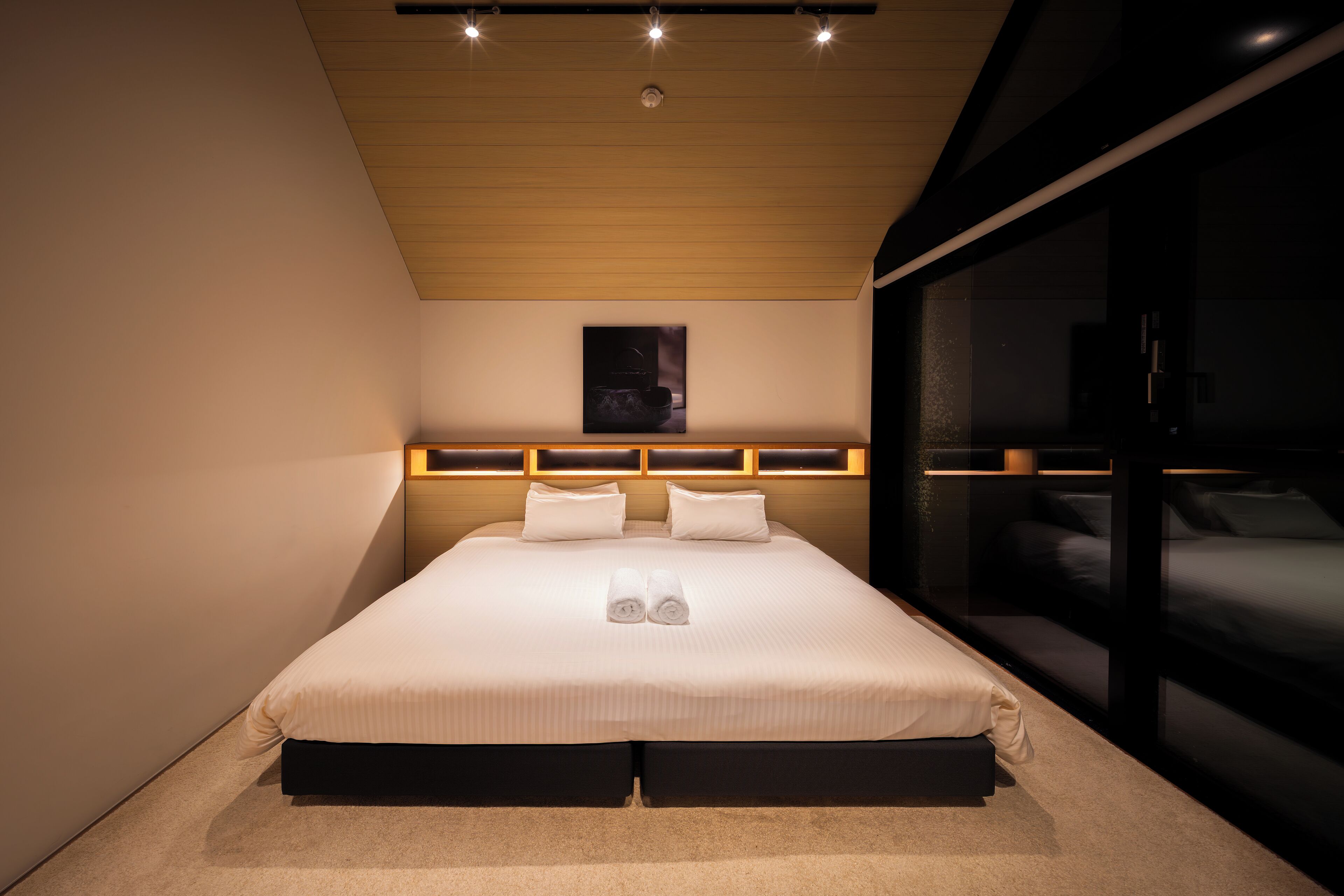 Un dormitorio moderno con una cama grande, cabecera con iluminación integrada, un ventanal amplio y una mesita de noche.