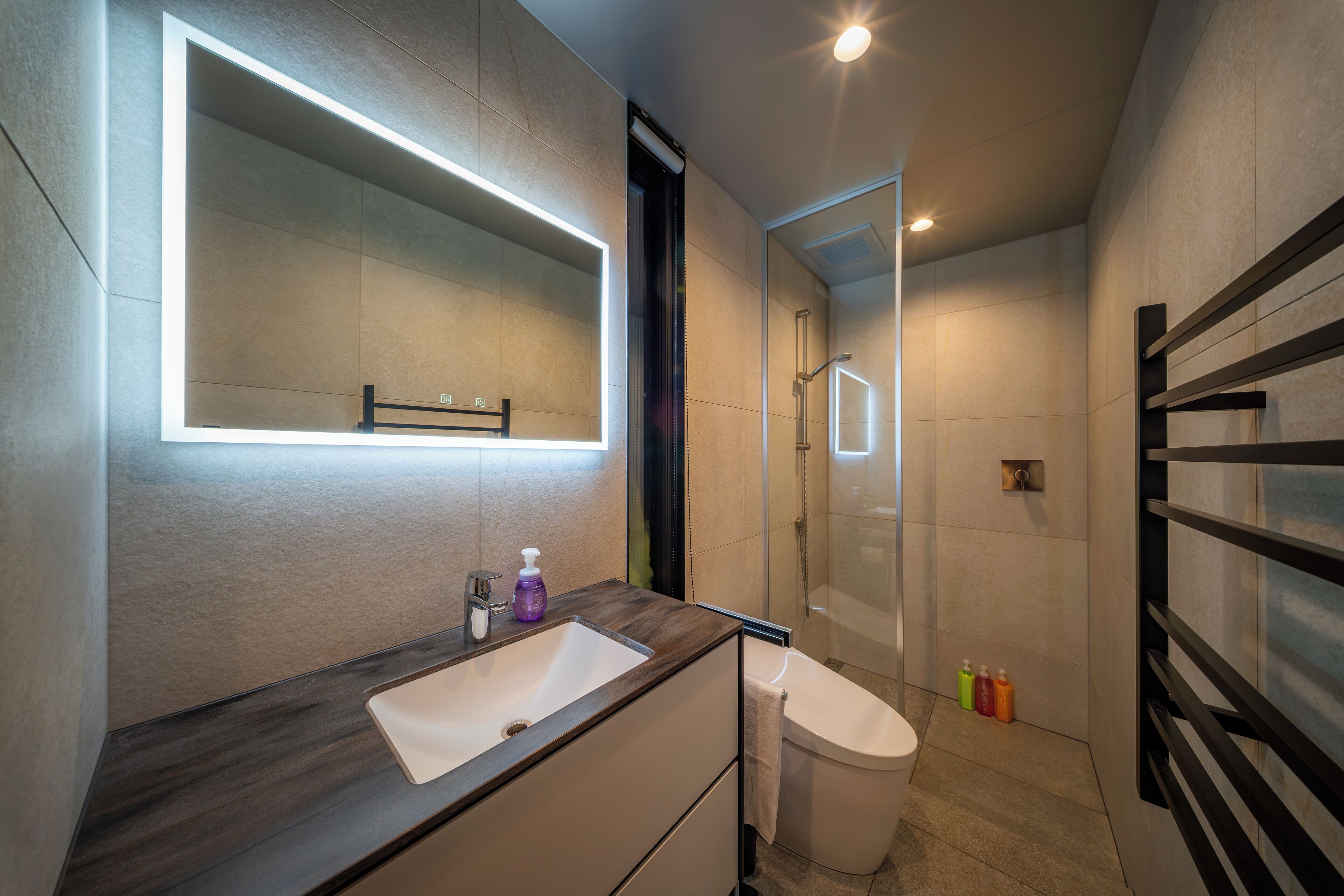A modern bathroom with a large mirror, a sink, a toilet, and a glass shower enclosure.