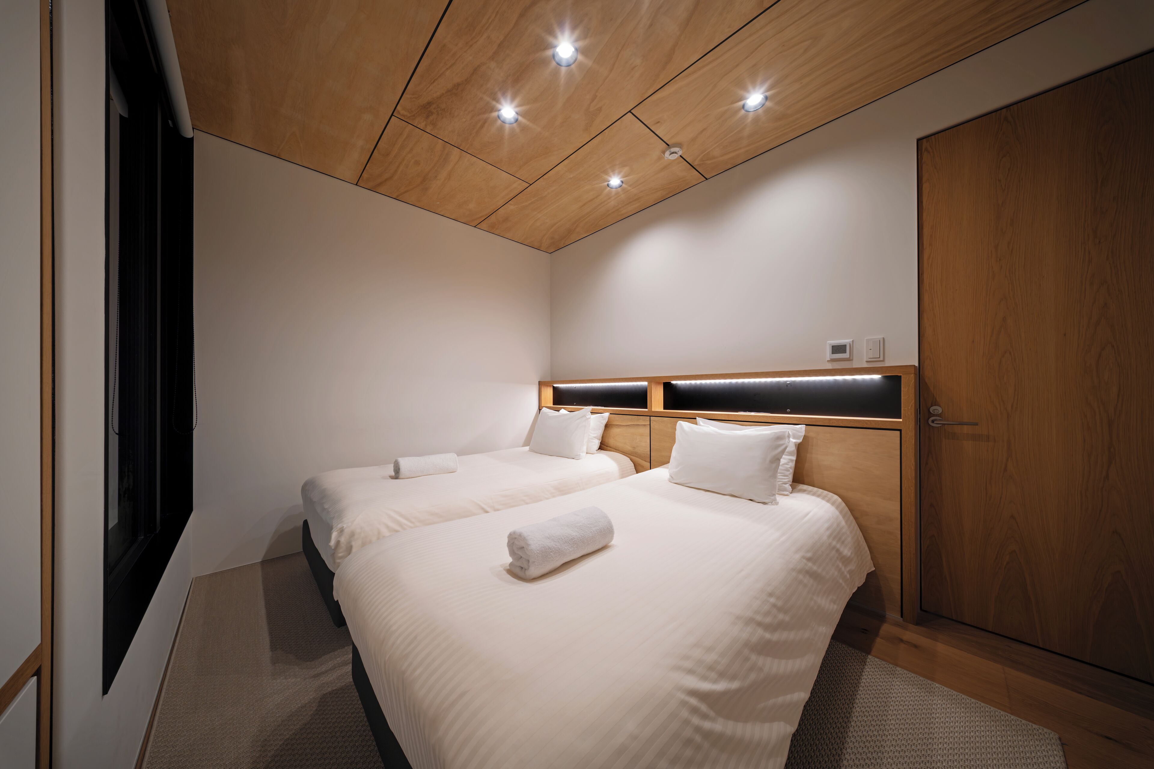 A modern hotel room with two beds, wooden ceiling, and a large wardrobe.