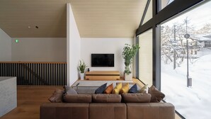Ein modernes Wohnzimmer mit einem großen Fenster, einem Flachbildfernseher, einer Holzbank und einem braunen Ledersofa.