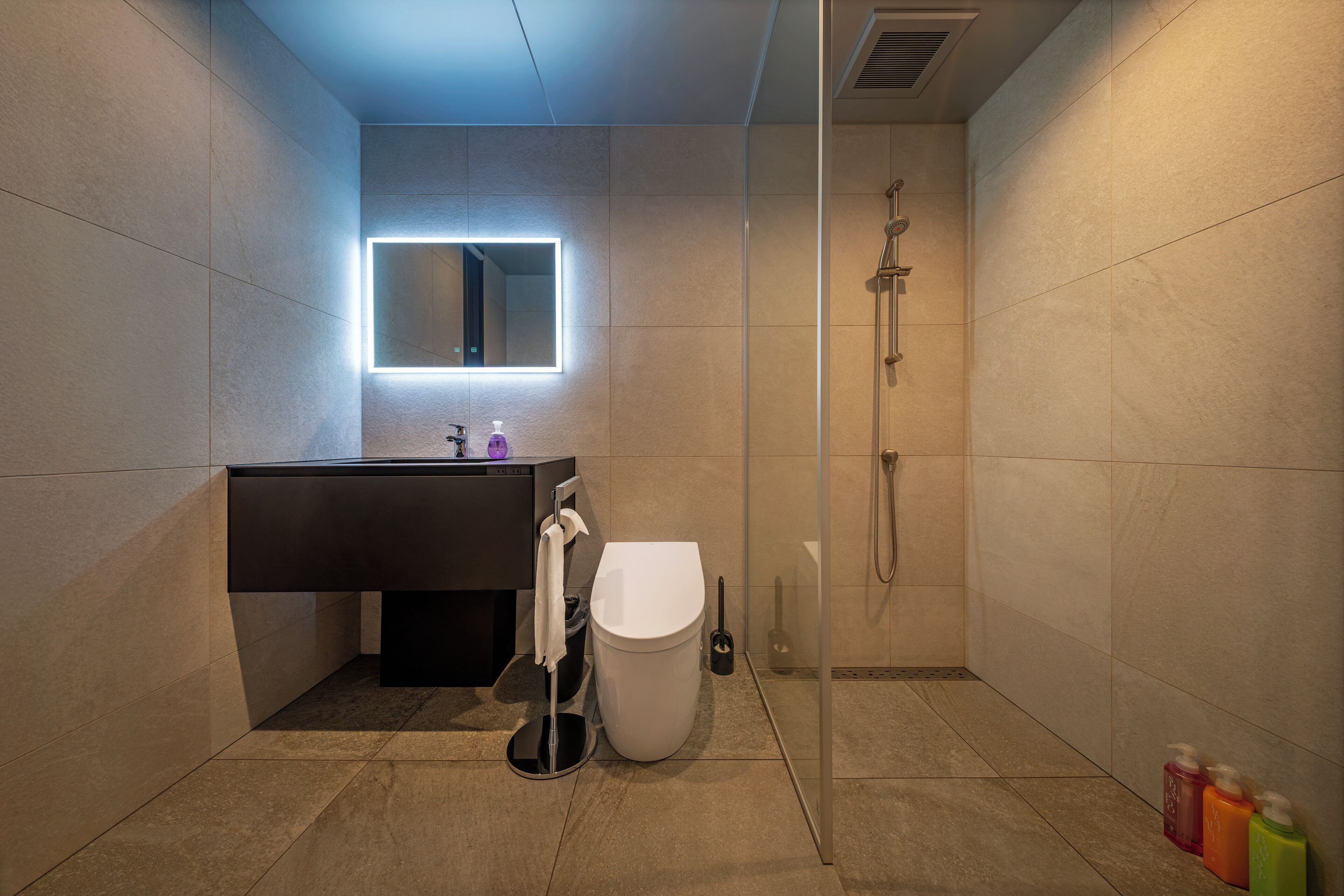 Un baño moderno con ducha de vidrio, inodoro blanco y tocador oscuro con espejo.
