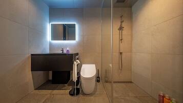 A modern bathroom with a glass-enclosed shower, a white toilet, and a dark vanity with a mirror.