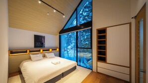 Ein modernes Schlafzimmer mit einem großen Bett, eingebauten Regalen und Blick auf verschneite Bäume durch große Fenster.