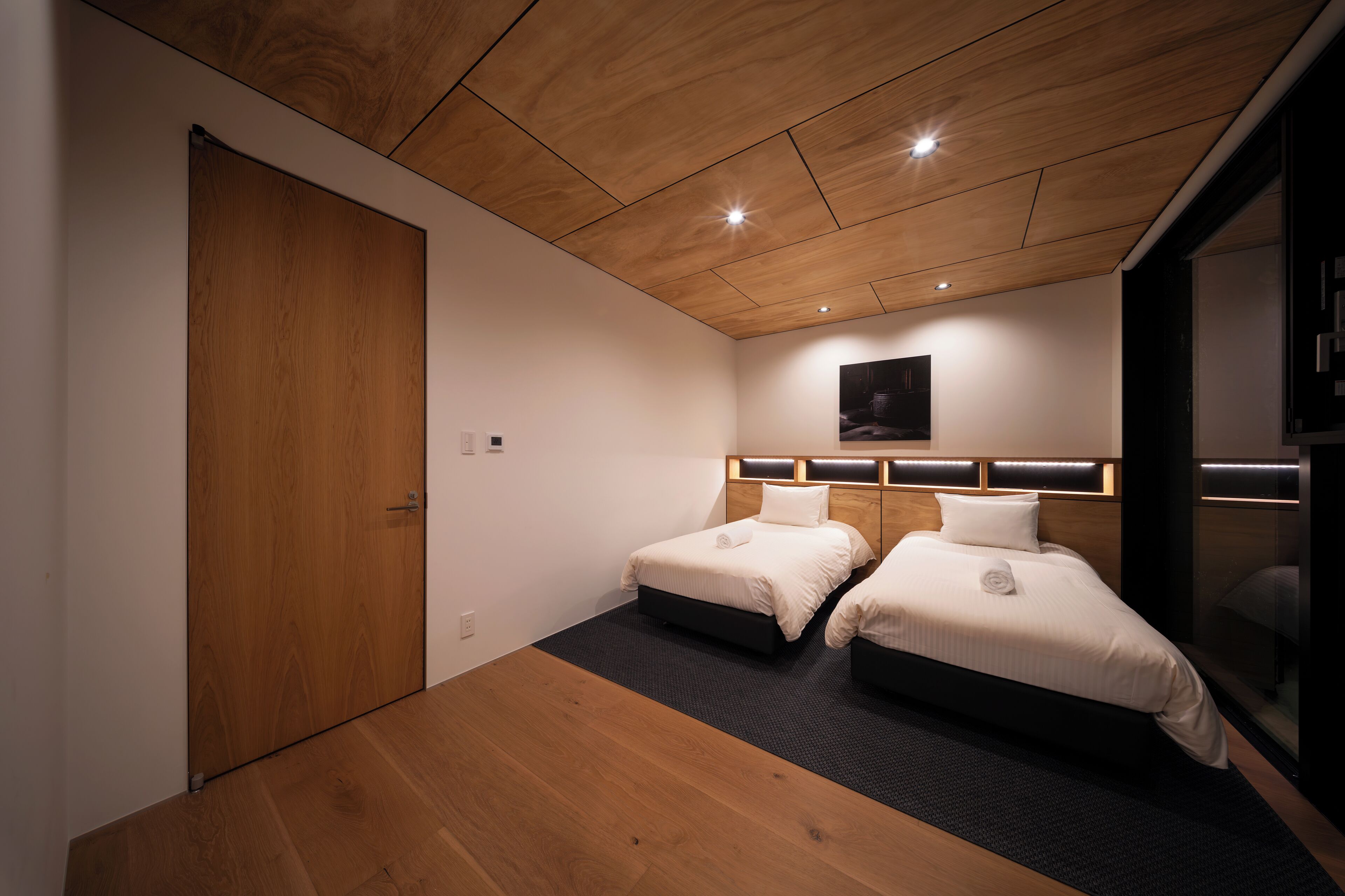 Una habitación de hotel moderna con dos camas, techo de madera y un ventanal grande.