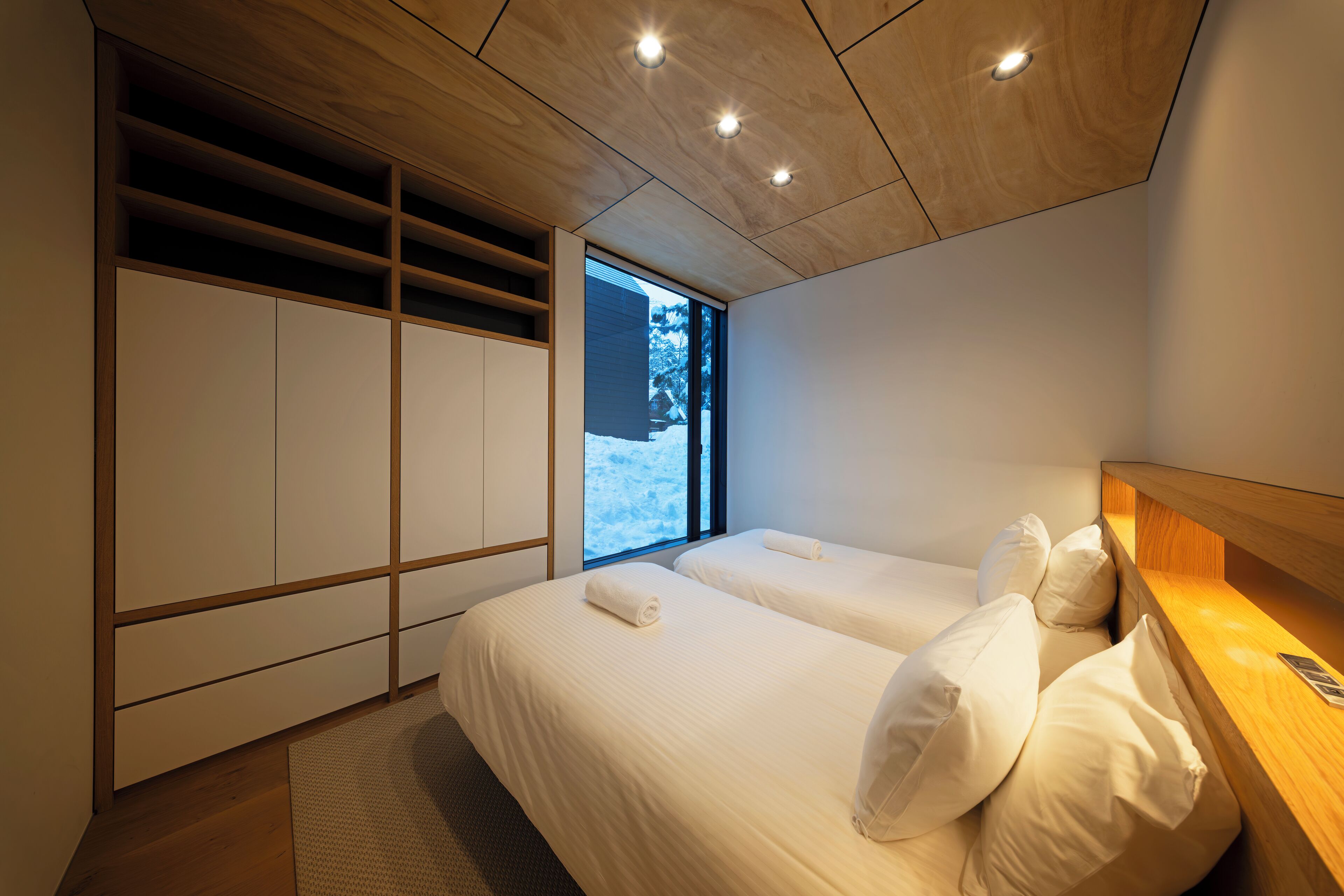 A modern bedroom with two beds, wooden ceiling, and a large window.