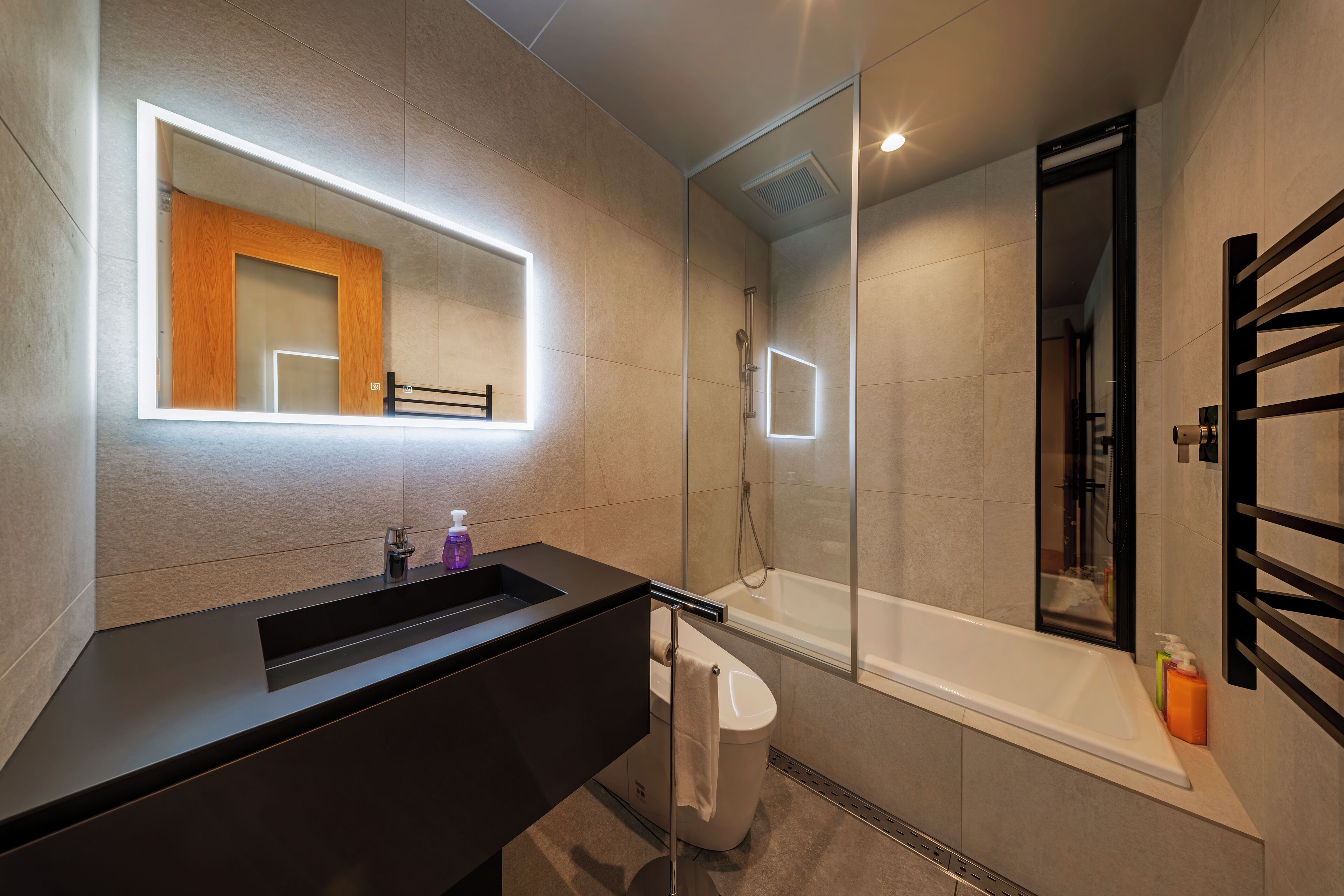 A modern bathroom with a black vanity, a glass-enclosed shower, and a large mirror with integrated lighting.