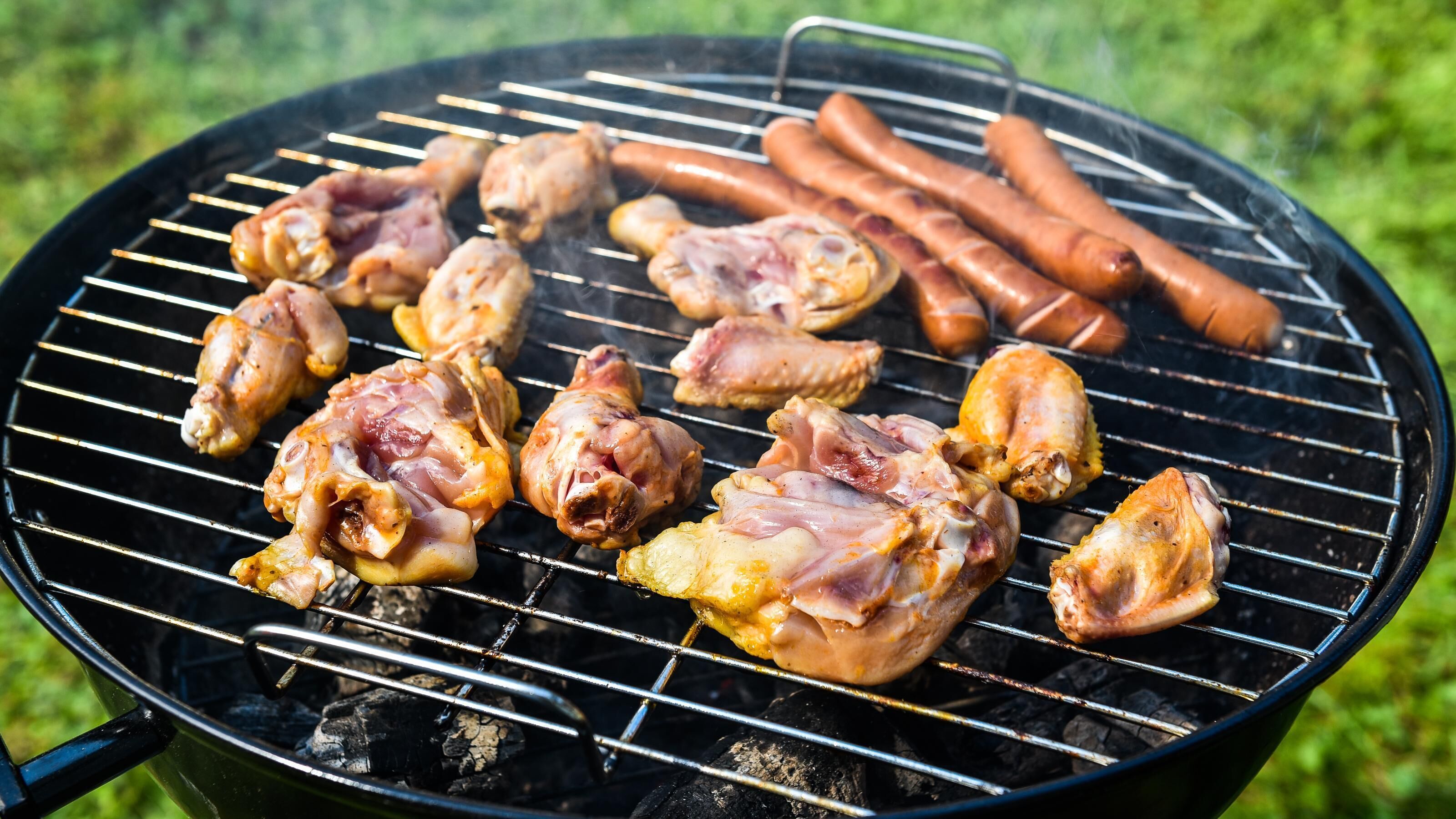 A grill with chicken and sausages being cooked.