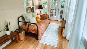 Quarto aconchegante com cama, mesa de cabeceira, luminária, janela e porta que dá para área externa.
