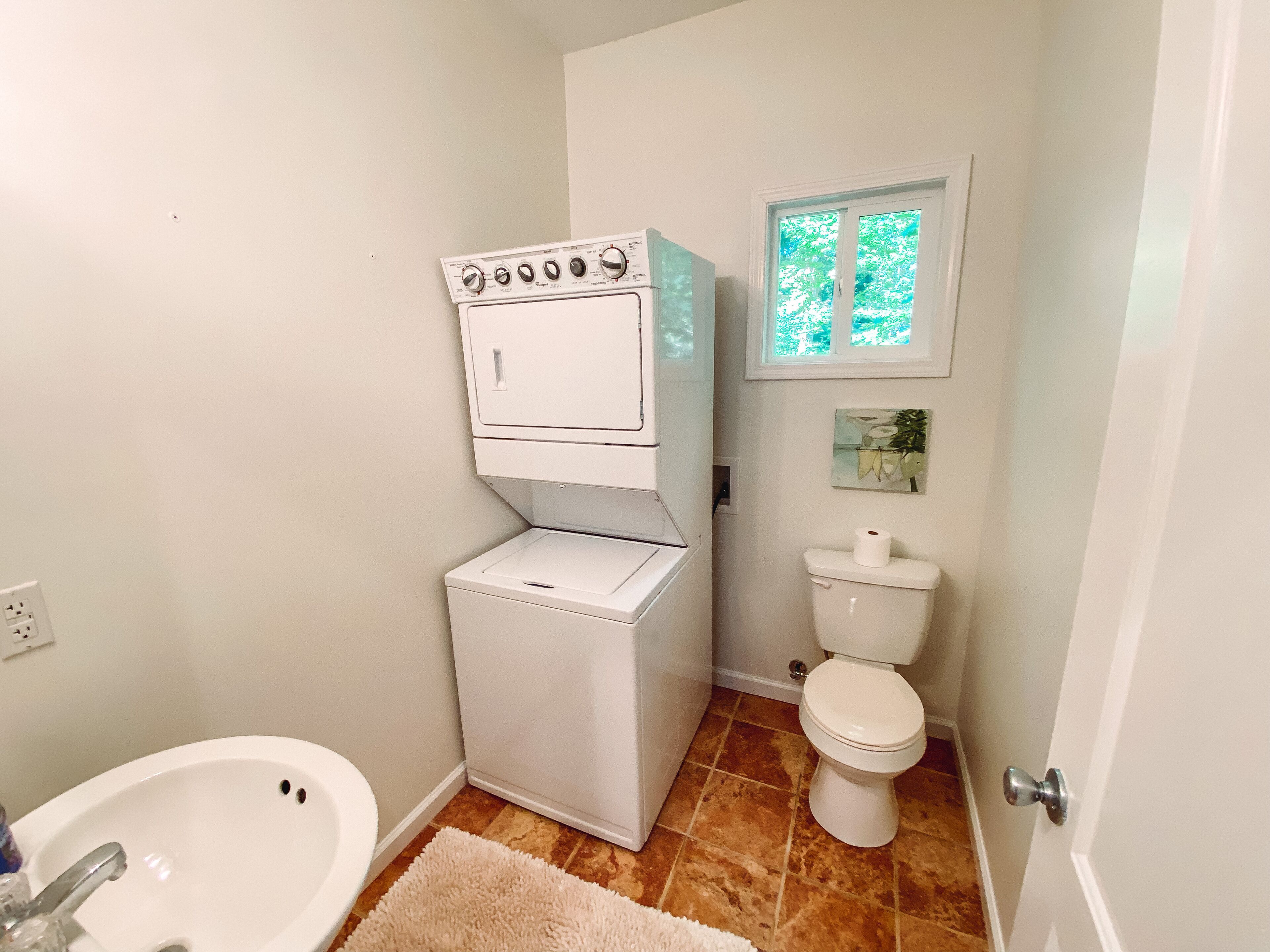 A compact bathroom with a white toilet, a white pedestal sink, and a white washing machine.