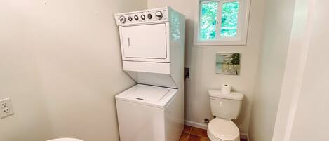 Un baño pequeño con inodoro blanco, lavamanos pedestal blanco y lavadora blanca.