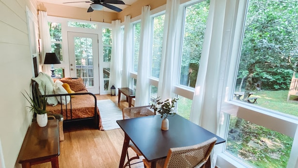 Quarto com piso de madeira, mesa de jantar com cadeiras, sofá e ventilador de teto.