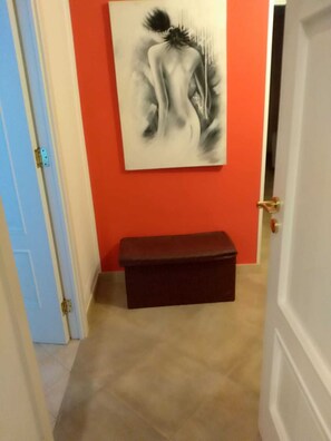 Um corredor com uma parede vermelha, um banco escuro e uma pintura de uma figura.