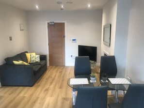 A modern living room with a sofa, two armchairs, a glass coffee table, and a flat-screen TV.