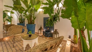 Ein Zimmer mit großen Kübelpflanzen, Korbmöbeln und einem gefliesten Boden.