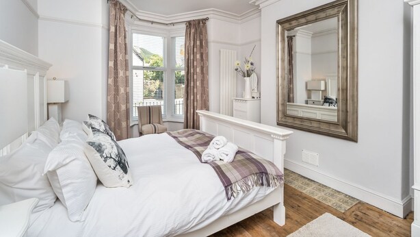 Een keurig opgemaakt slaapkamer met een groot bed, nachtkastje, spiegel en een raam met gordijnen.