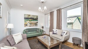 Een woonkamer met een bank, een groene fauteuil, een glazen salontafel en een lamp.