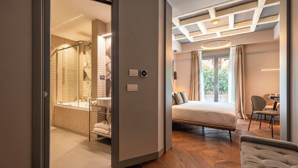 A modern hotel room with a shower, a bed, a seating area, and a view of the outdoors. - Loly Boutique Hotel (Rome)