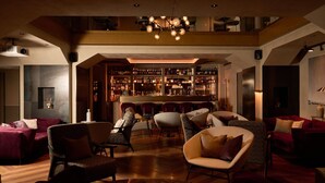 A spacious lounge area with a bar in the background, featuring multiple seating options and a high ceiling with a chandelier. - Loly Boutique Hotel (Rome)
