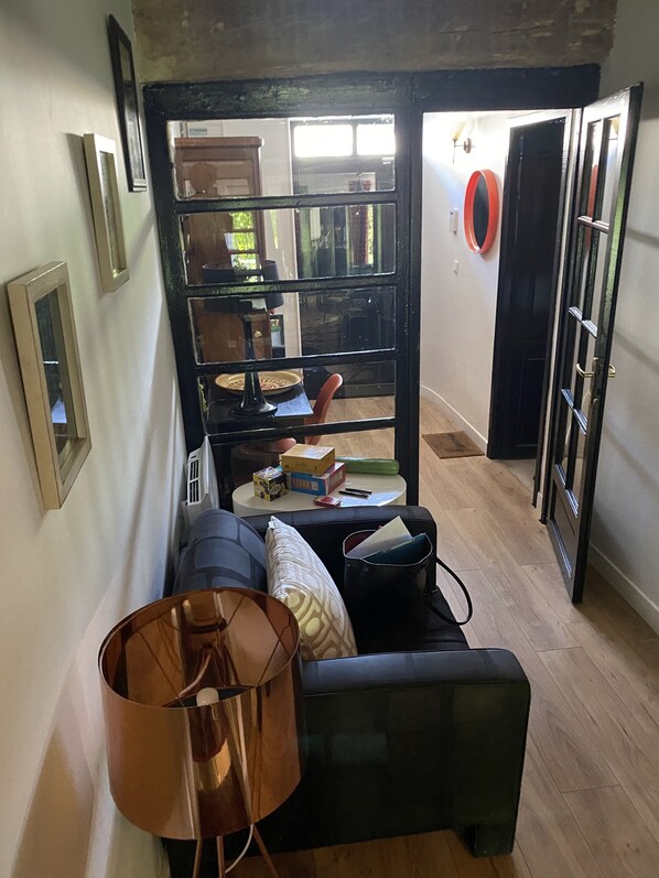 A compact living space with a sofa, a lamp, and a small table with items on it. A door leads to another room.