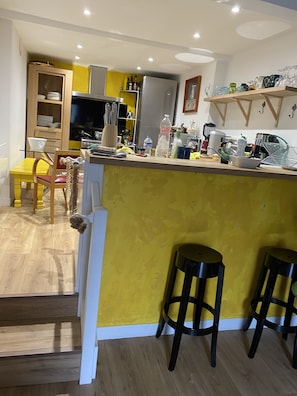 Eine moderne Küche mit gelber Akzentwand, Holzbarhocker und einem Essbereich mit gelben Stühlen.