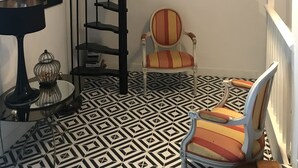 A spiral staircase, a chair, a table with a lamp, a framed picture, and a patterned floor.