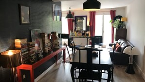 A modern living room with a dark wall, a dining area with a table and chairs, and a sofa with a lamp.