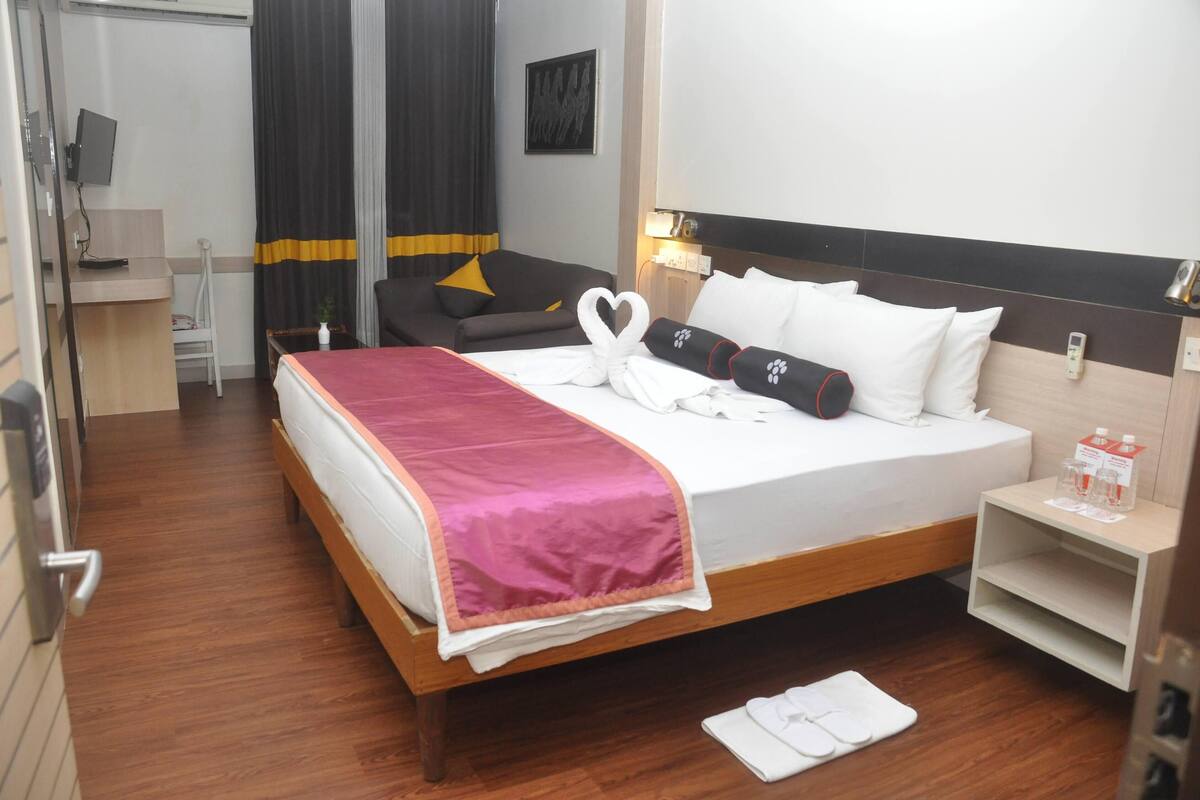 Una habitación de hotel con cama, escritorio, silla, televisor y estante en la pared.