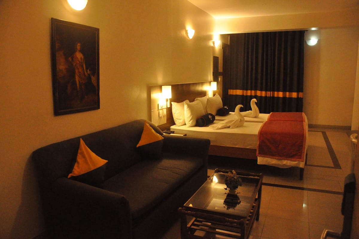 Una habitación de hotel con cama, sofá, mesa de centro y un cuadro en la pared.