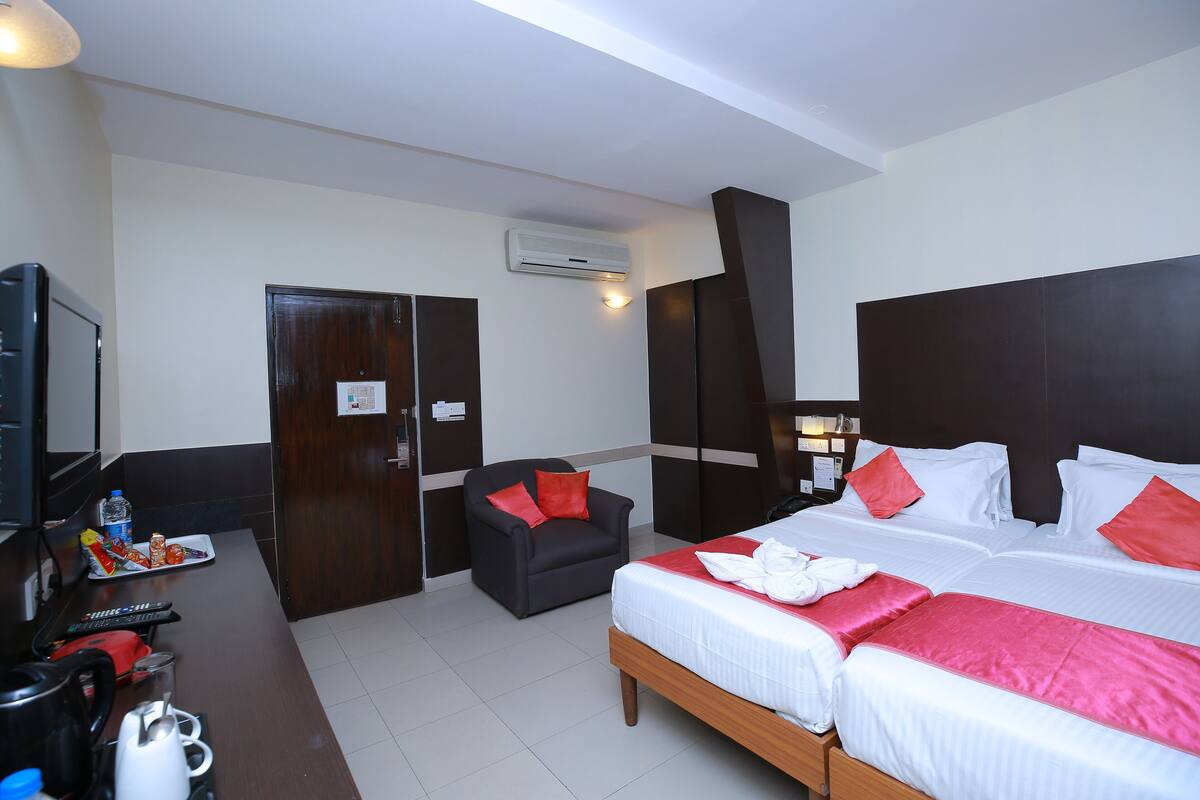 Habitación de hotel con una cama grande, un escritorio con cafetera, una silla y un televisor.