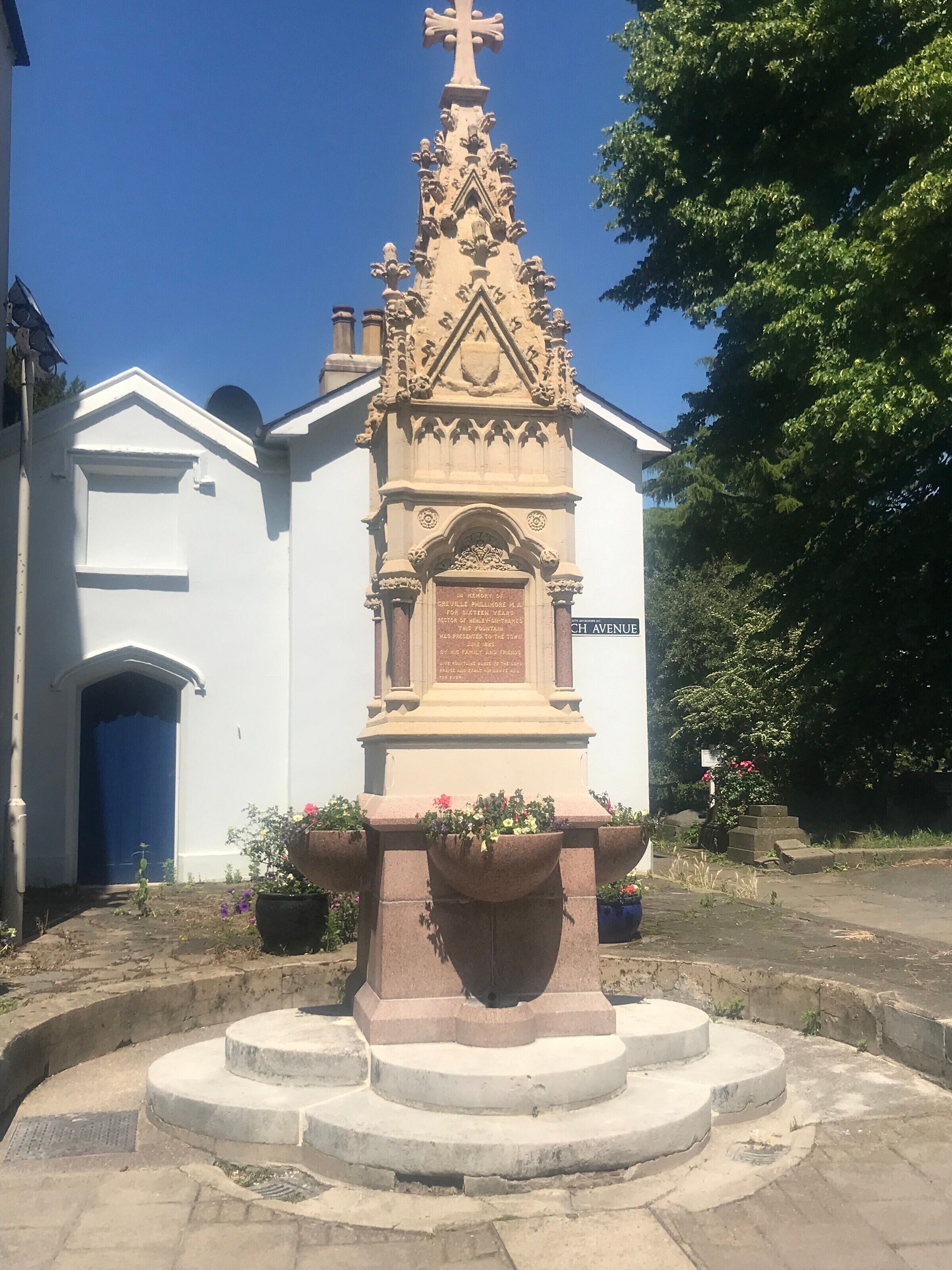 A church with a stone monument in front, a white building with a blue door, and a clear blue sky.