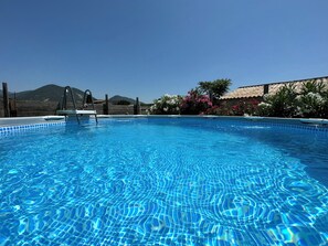 Une piscine d’un bleu éclatant, dotée d’un escalier, entourée de plantes et avec une montagne en arrière-plan.