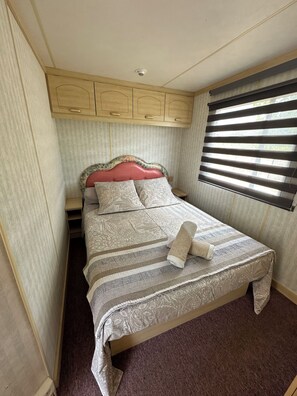 Une chambre à coucher comprenant un lit, une tête de lit, une fenêtre avec des stores et une caméra de surveillance fixée au plafond.