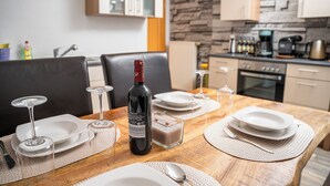 A dining table set with plates, glasses, and a bottle of wine, with a kitchen in the background. - Fe-Wo Gold-Blick*** (Korbach)