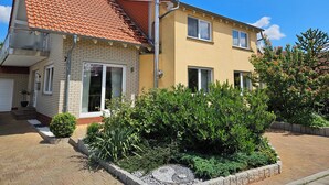 A two-story house with a red-tiled roof, brick facade, and a small garden area with various plants. - Fe-Wo Gold-Blick*** (Korbach)