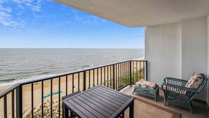 A balcony with a view of the ocean, a table, and two wicker chairs.