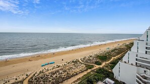 A beach view with a clear sky, sandy beach, and a white building with multiple floors.