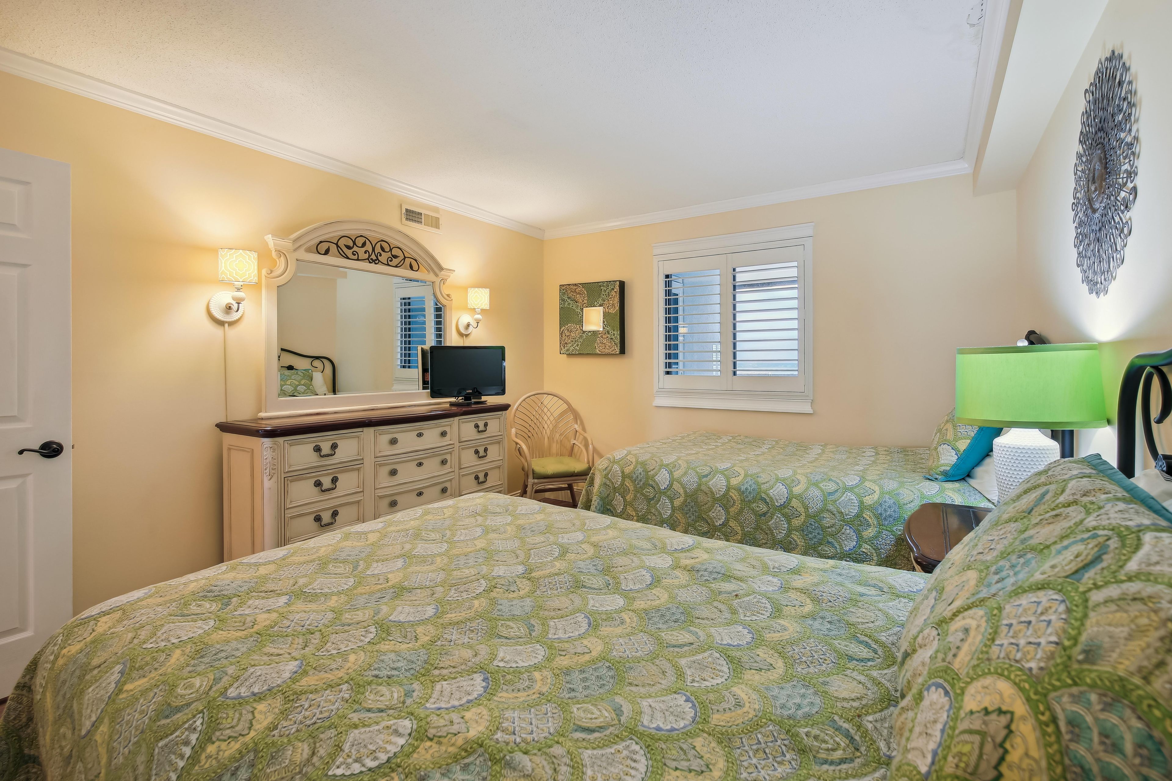 A bedroom with two beds, a dresser, a television, and a window with blinds.
