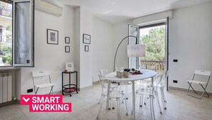 A modern, well-lit room with a round table and clear chairs, a standing lamp, and framed inspirational quotes on the wall. - Shelley Apartments - Sun by Wonderful Italy (Genova)