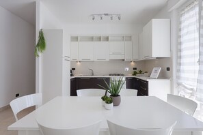 Eine moderne Küche mit weißen Schränken, einer zentralen Kochinsel mit Pflanze und einem Essbereich mit weißen Stühlen.