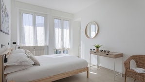 Una camera da letto con un letto, un comodino con uno specchio, una sedia e una finestra con tende.