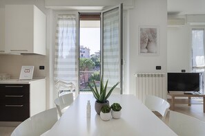 Een moderne keuken met witte kasten, een eettafel met stoelen, een potplant en een lijst met foto aan de muur.