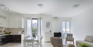 A modern apartment with a kitchen, dining area, and living room, featuring a balcony and a TV.
