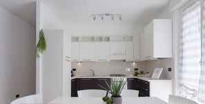 A modern kitchen with white cabinets, a central island, and a dining area with a white table and chairs. There is a potted plant on the island and a small plant on the countertop.