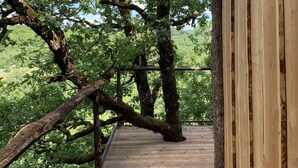 A wooden deck with a metal railing, surrounded by trees and a clear sky. - Wooden tree house (Salvagnac-Cajarc)