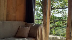 A wooden interior with a sofa, a table with candles, and a view of greenery outside. - Wooden tree house (Salvagnac-Cajarc)